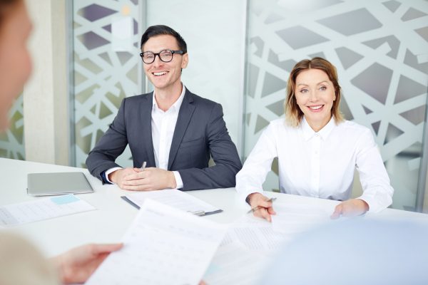 Two confident employers talking to applicants during interview in office